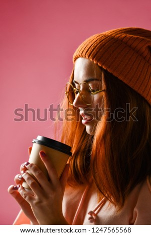 Close-up side photo of pretty red head woman in warm clothes drinking hot tea, isolated on pink background