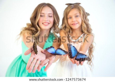 Two girls in dresses holding alive tropical butterflies