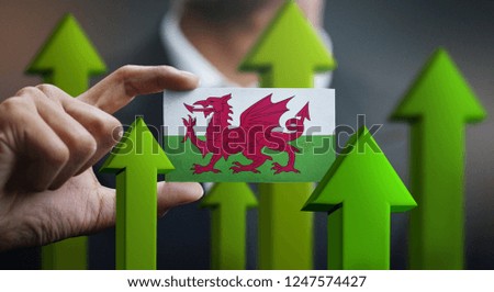 Nation Growth Concept, Green Up Arrows - Businessman Holding Card of Wales Flag 