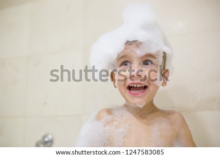 A Boy is taking a bath with bath foam on his head and face close up