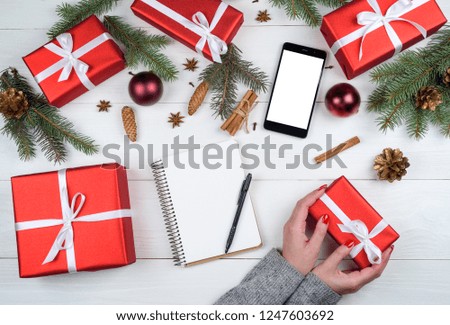 Christmas gift wrapping background, copy space. Woman with red manicure holding in hands red box with white ribbon bow, top view. Winter holidays concept, flat lay. Blank notebook
