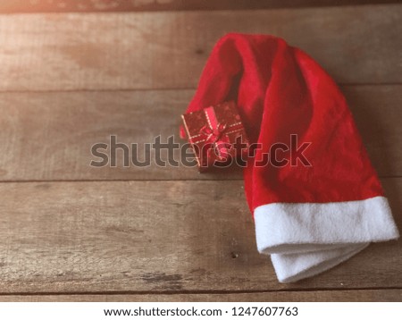 Red christmas hat,like a Santa Claus,and Red Gift Box on wood empty,dark tone,with copy space.Selective focus,rural style,with lens flare.Decorative series for merry christmas and new year festival.