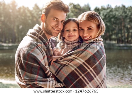 Young parents hugg their little daughter in autumn forest near the lake.