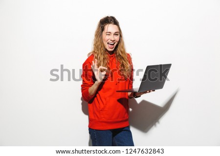 Image of modern woman 20s wearing red sweatshirt holding laptop isolated over white background