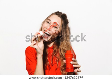 Image of european woman 20s wearing red sweatshirt blowing soap bubbles isolated over white background