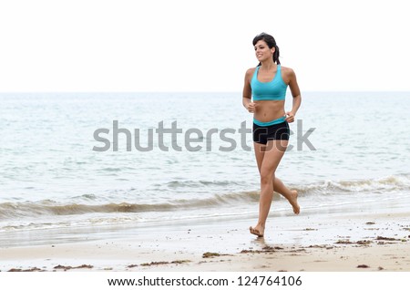 Attractive young woman running fast on beach on a cloudy day in summer. Fitness cheerful model jogging and workout near the sea.