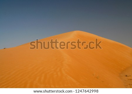Orange-yellow sand dunes forming a cone against blue sky in Oman desert