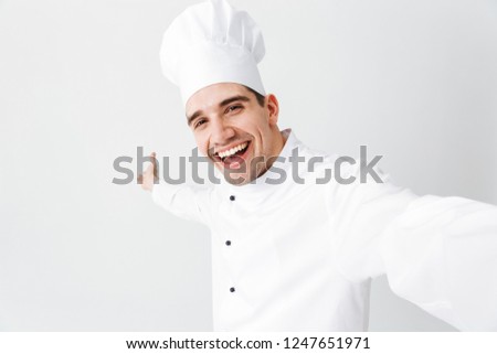 Happy chef cook wearing uniform standing isolated over white background, taking a selfie