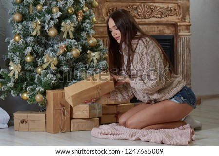 beautiful woman on her knees near the Christmas tree and fireplace picks up a Christmas gift
