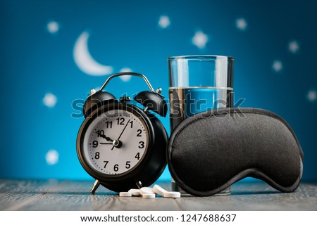 Alarm clock, mask, sleeping pills and glass of water. Fighting with insomnia for a good night rest. Royalty-Free Stock Photo #1247688637