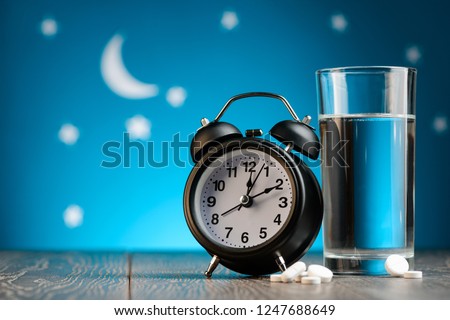 Alarm clock, pills and glass of water on a bedside table. Insomnia, treatment for sleepless nights. Royalty-Free Stock Photo #1247688649
