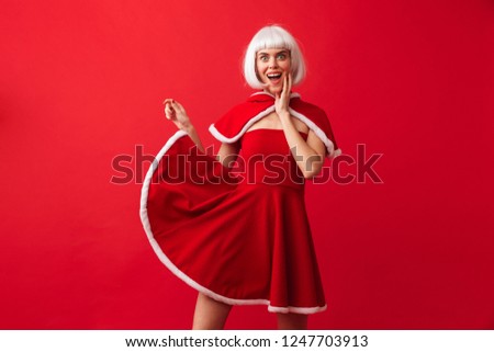 Beautiful young girl wearing red Christmas dress standing isolated over red background, posing