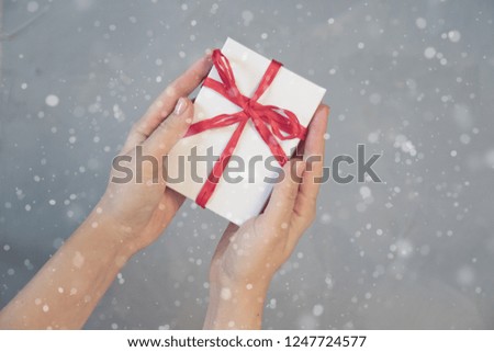 Woman hands holding present box with red bow on pastel pink background with multicolored confetti. Flat lay