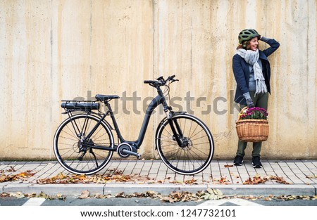 Active senior woman with electrobike standing outdoors in town, leaning against bike.