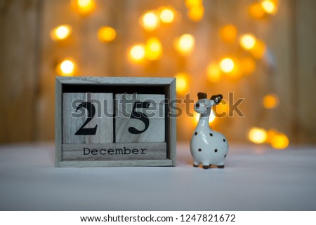 Cube wooden calendar showing date on 25th December with ceramic reindeer figurine over bokeh background. Advent calendar, Christmas background, Copy space