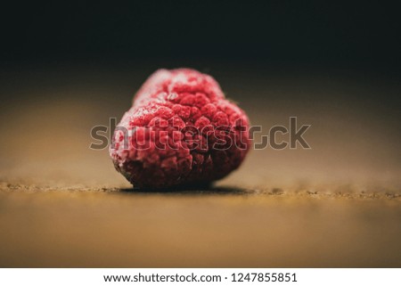 Close up picture of raspberrie on old vintage wooden board in a dark black background key lighting a berry, macro close up
