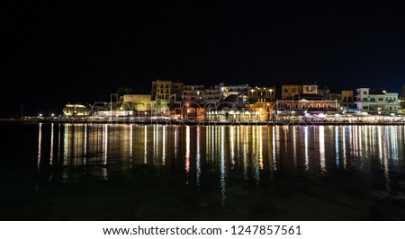Night view over Chania harbor with reflections on the water. Colorful light strips contrasting deep black surface of the bay. Evening in Greek island Crete.
