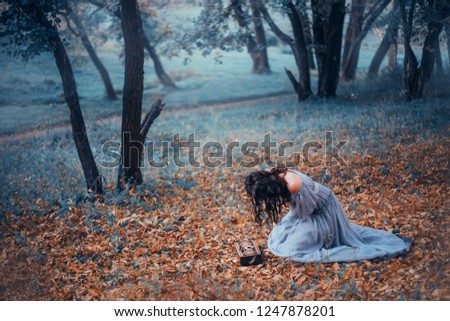 dark-haired girl in a long, light gray, old-fashioned dress, sits on cold ground covered with autumnal fallen leaves, in a dark forest, crying over Pandora’s open box. no face on art photo, depersia
