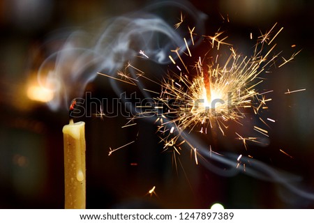 sparkler burns against a dark background. Near the smoking candle