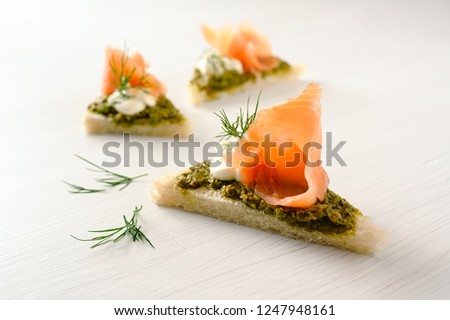 canapes with smoked salmon, pesto, cream and dill garnish on a light background with copy space, selected focus, narrow depth of field