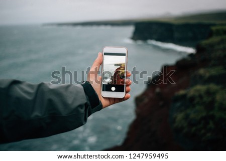 Adventurer, hiker or tourist holds out smartphone with photograph of amazing epic rough and beautiful icelandic landscape. Travel blogger or social media influencer explores place less travelled