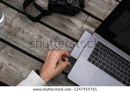 Top view on designer wooden table, photographer takes out memory card from camera to insert it in multifunctional futuristic card reader or cable adaptor for new laptop for data transfer