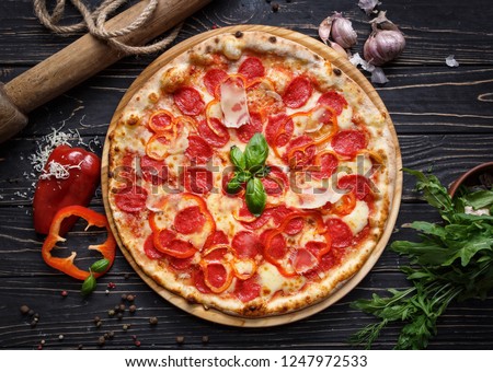 Fragrant pizza with sausage and peppers. Concept promotional flyer. Pizza on a black wooden background among spices