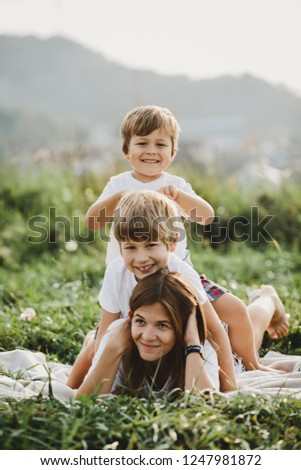 Charming young mother has fun with her little sons lying on a plaid on green grass