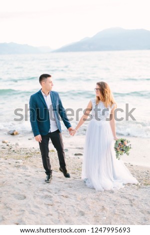 Beautiful happy wedding couple of groom and bride walking holding hands on the pier near the lake. Garda Lake, Italy. Wedding day concept