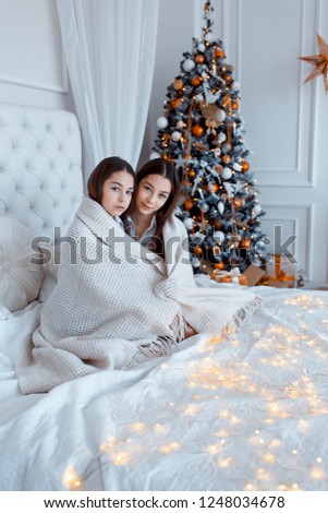 Girls twins in front of the fir-tree. New year's eve. Christmas. Cozy holiday at the fir-tree with lights and gold decor.