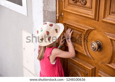 little girl with summer hat knocking on wooden door