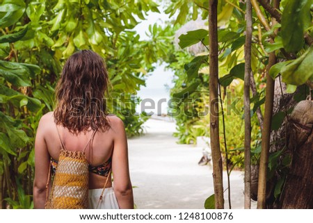picture from back of a girl walking on a path to the beach. Island hopping concept. Maldives