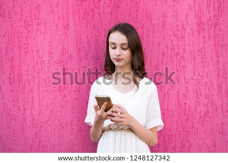 Young attractive female using mobile smartphone in white dress. Isolated on pink bakcground