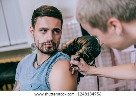 Starting new tattoo. Handsome bearded young man getting new tattoo by his well-known female artist