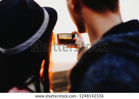 Back view of young couple using smartphone to take photo of magnificent sundown in nature.Unrecognizable couple taking picture of sundown