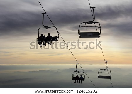 Ski-lift transports skiers to the top of the mountain and the sun goes down