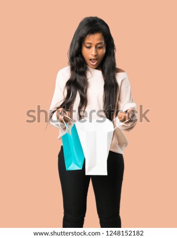Young afro american woman surprised while holding a lot of shopping bags on isolated brown background