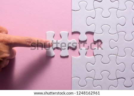 Close up of hand placing the last jigsaw puzzle piece on pink background. Business and team work concept.