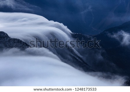 Cloud Waterfall, Abstract landscape image - Mountains and Valleys, Soft Fluffy clouds spilling over a mountain ridge into the valley below. Soft ghostly blue lighting, artistic nature photography