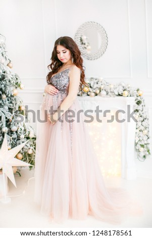 Pregnant woman with hands on belly under christmas tree.