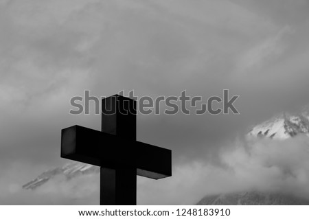 Black and white close up  silhouette of big  black Greek cross  in front of  foggy and snowy mountain peaks. Grief, loss, sorrow  and sadness. Memories and remembrance from the one who you left behind