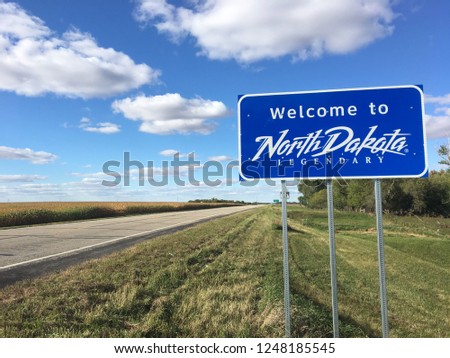 Welcome to North Dakota sign at state line with highway and cloudy sky in background