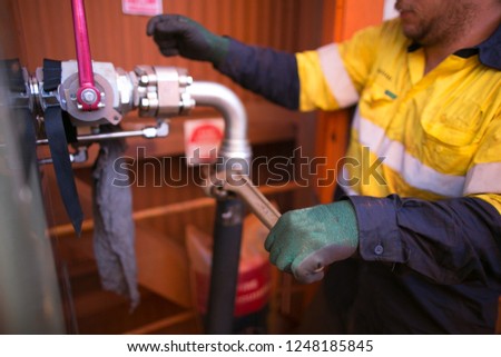 Picture of male miner hand plumber wearing a industrial glove performing fastening hydraulic hose with pipe wrench into a corner connector construction mine site, Perth, Australia      