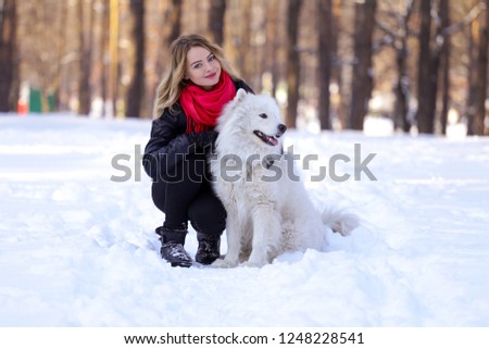 Beautiful young girl with a Samoyed dog in the winter forest on the snow
