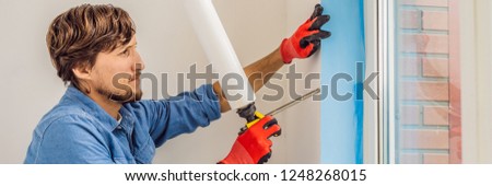 Man in a blue shirt does window installation BANNER, LONG FORMAT