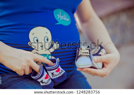Pregnant woman hold hands over belly and socks with shoes for newborn