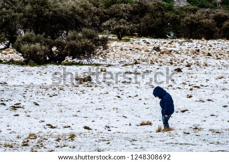 A boy with blue down jacket standing on the ground covered with white snow.
