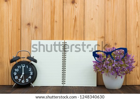 Office supplies or office work essential tools items, notebook and alarm clock with little tree and glasses on the wood.