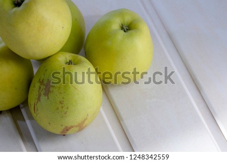Many green apples on a shelf. A white, wooden background.