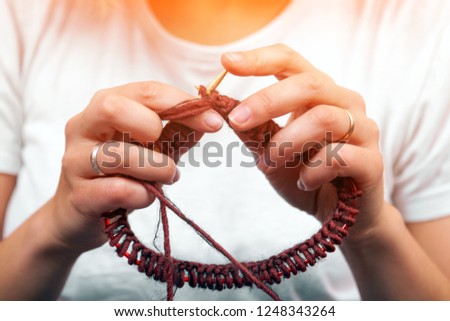 Close-up of a dark-haired beautiful woman smiling and knitting with knitting crochet from a natural woolen thread a  brown hat , a woman shows how to knit correctly